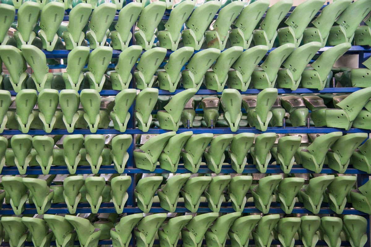 Green shoe lasts arranged in rows on blue shelves—the foundation of the Pas shaping process in Sioux shoe manufacturing.