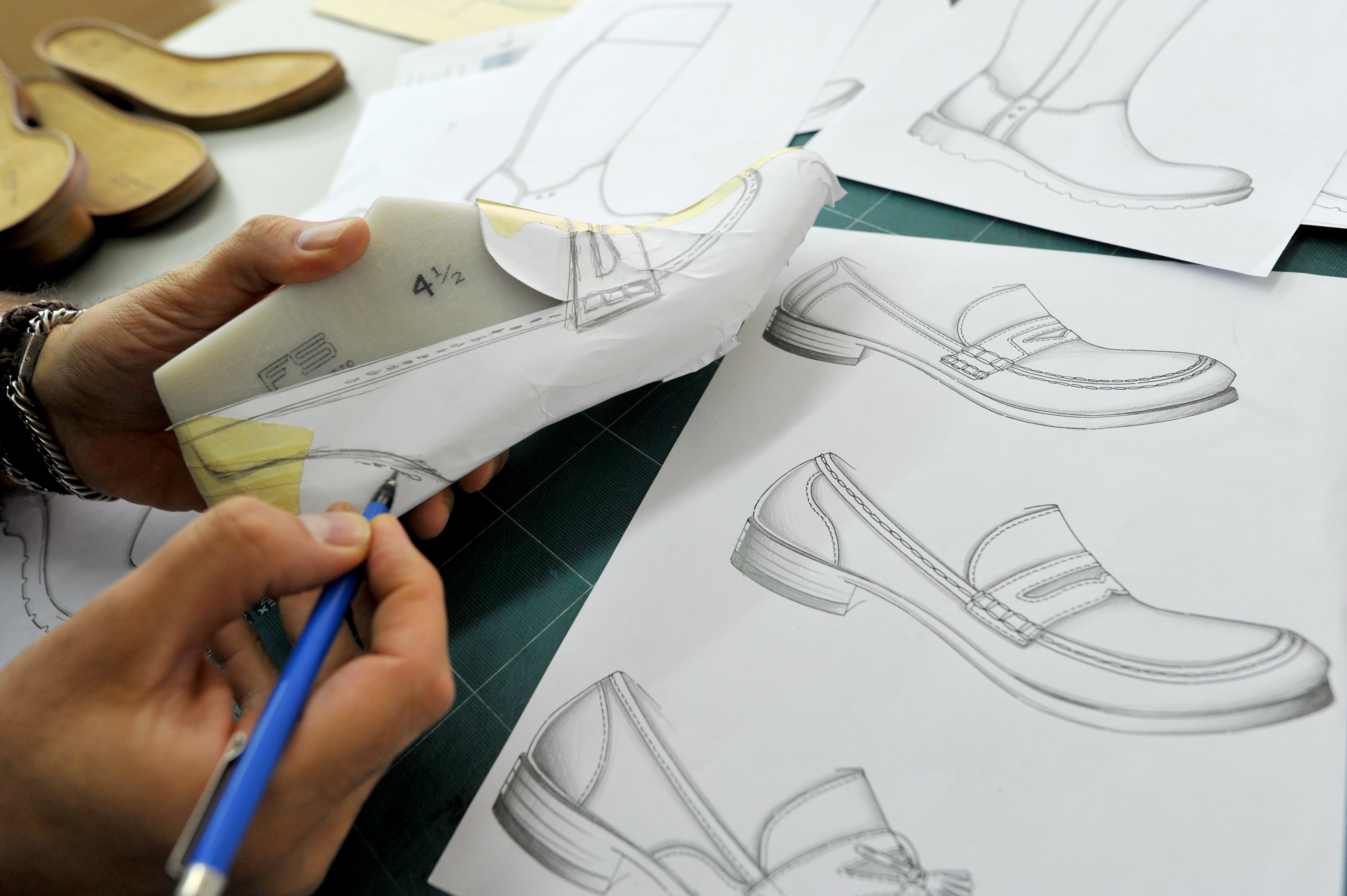 Hands are sketching a shoe design on a last; next to them are technical sketches for the Sioux model development.