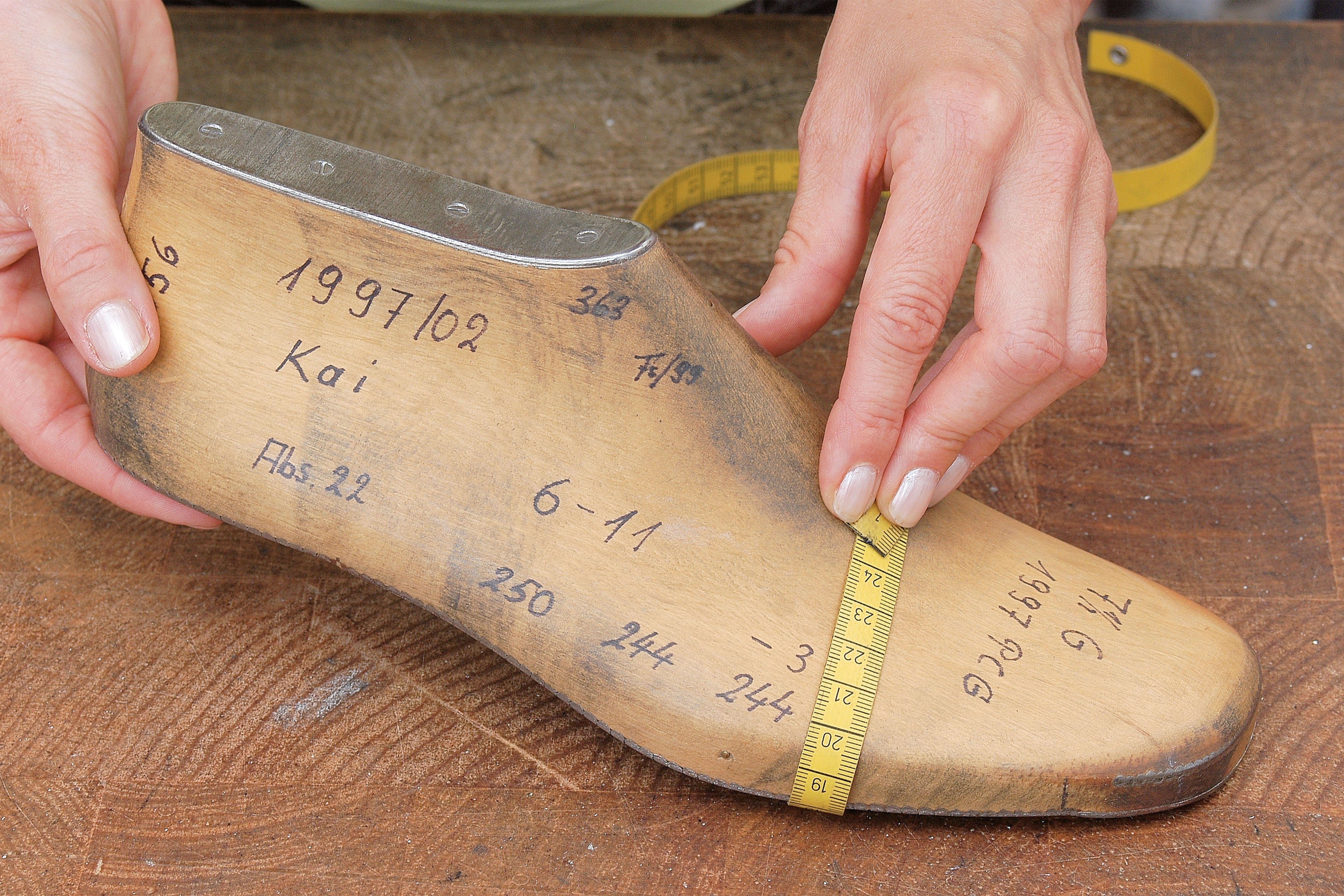Measuring a wooden shoe last with a measuring tape to determine the shoe width.