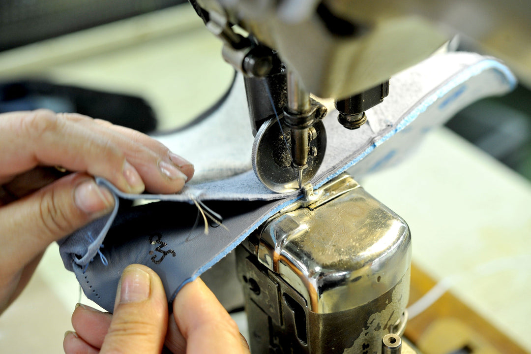 Hands guide a piece of leather under the sewing machine—precise craftsmanship on a shoe upper in the stitching department.