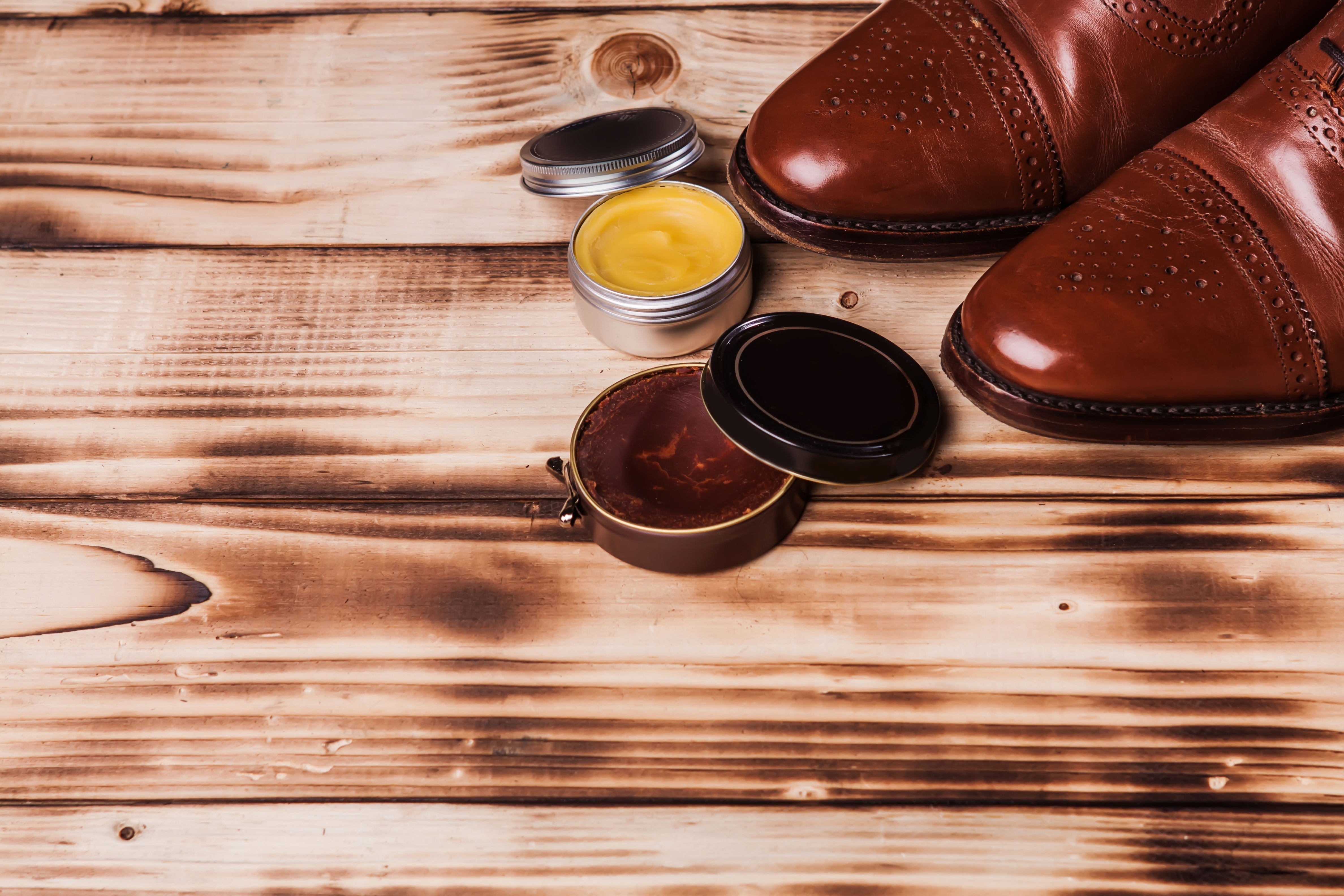 Braune Lederschuhe mit geöffneter Schuhcreme und Schuhwachs auf einem Holztisch zur Pflege von Glattleder.