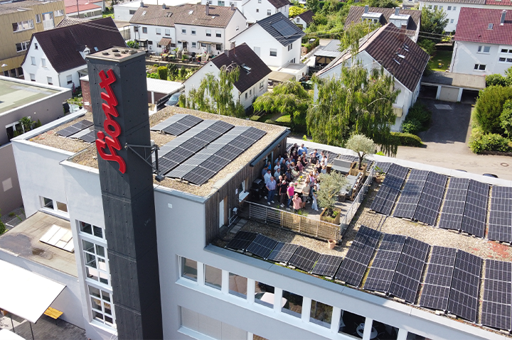 Luftaufnahme des Sioux Firmengebäudes in Walheim mit großem Sioux Logo, Solaranlagen auf den Dächern und Mitarbeitern auf der Dachterrasse.